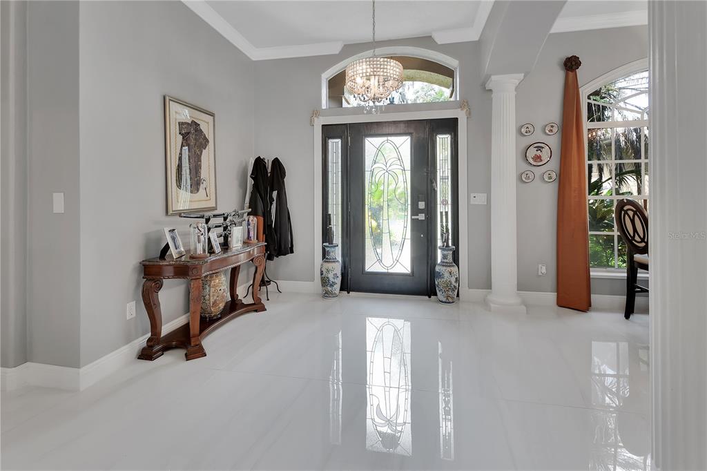 A bright foyer features white tile floors, a dark front door, and a crystal chandelier — 6241 PALOMINO CIRCLE, PORT ORANGE, FL