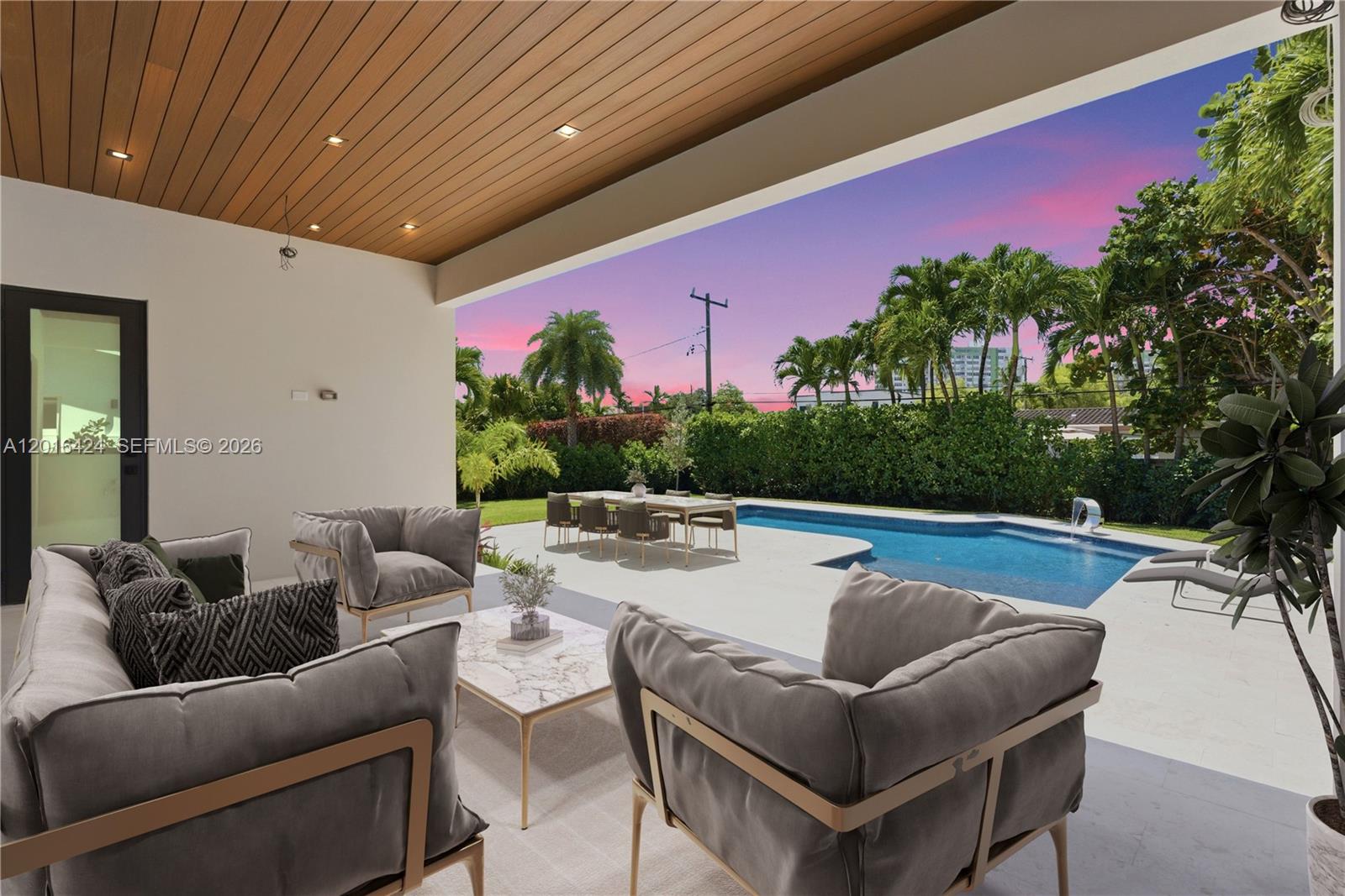 A covered patio features modern outdoor furniture overlooking a swimming pool and a landscaped backyard — 1940 Alamanda Dr, North Miami FL 33181, NORTH MIAMI, FL