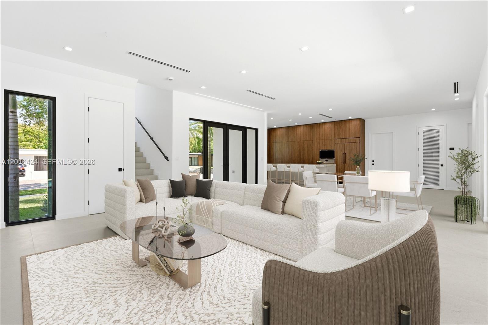 A modern living room features a large sectional sofa, a glass coffee table, and wood cabinetry — 1940 Alamanda Dr, North Miami FL 33181, NORTH MIAMI, FL