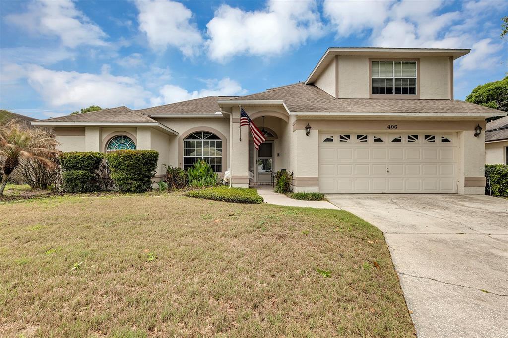 A two-story suburban house with a beige stucco exterior, a two-car garage, and a lawn — 406 STERLING LAKE DR, OCOEE, FL