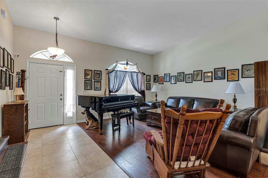 A living room features a grand piano, dark wood flooring, leather furniture, and framed wall art — 406 STERLING LAKE DR, OCOEE, FL