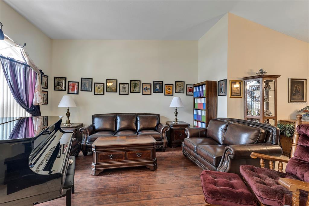 A living room features a grand piano, leather sofas, a coffee table, and framed wall art — 406 STERLING LAKE DR, OCOEE, FL