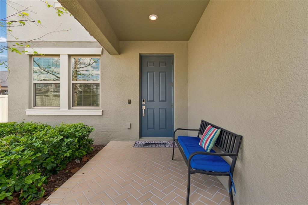 A covered front porch features a blue door, a black metal bench, and herringbone pavers — 8960 SHADYSIDE LANE, LAND O LAKES, FL
