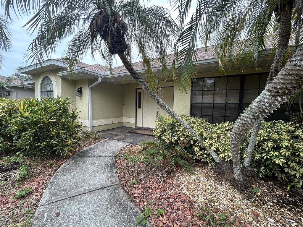 A concrete walkway leads to the front entrance of a house with palm trees — 1612 GULF BEACH BOULEVARD, TARPON SPRINGS, FL