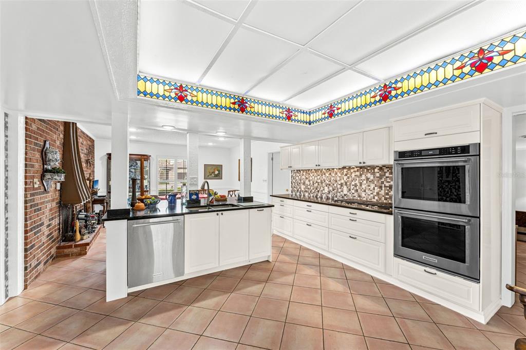 A kitchen features white cabinets, stainless steel appliances, a tiled backsplash, and a stained-glass ceiling — 1790 BAY SHORE DRIVE, COCOA BEACH, FL