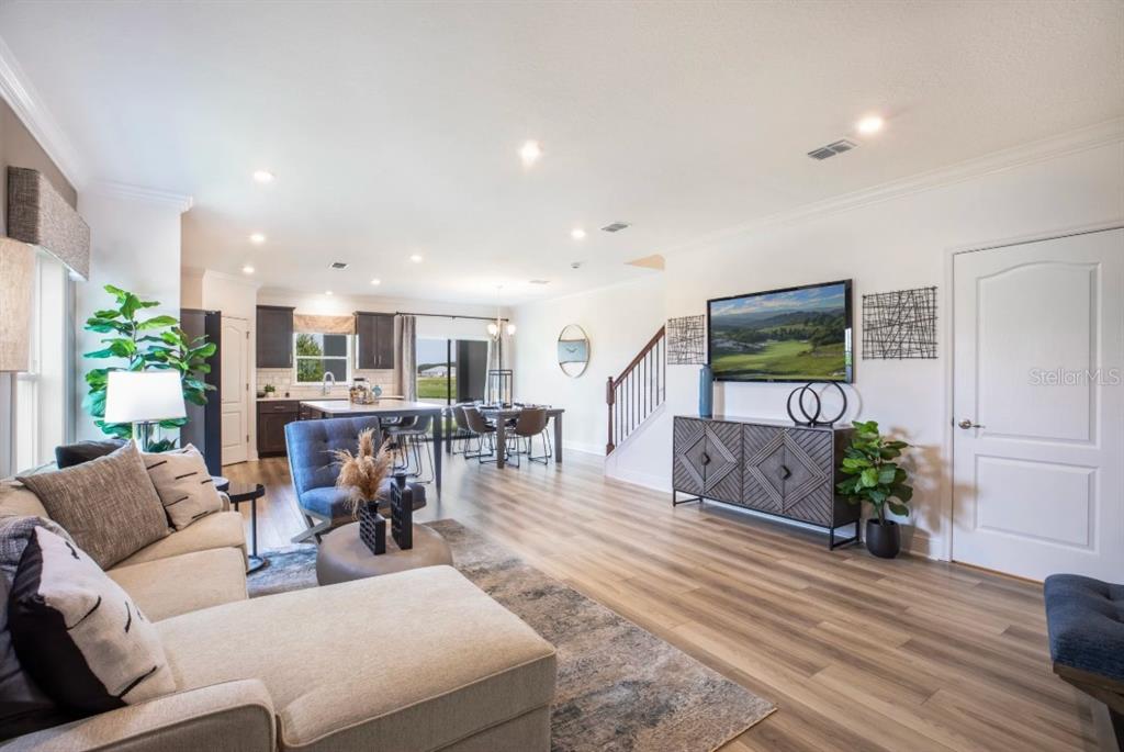 An open-concept living room features light wood flooring, a sectional sofa, and a wall-mounted television — 32107 EASTERN REDBUD BRANCH, SAN ANTONIO, FL