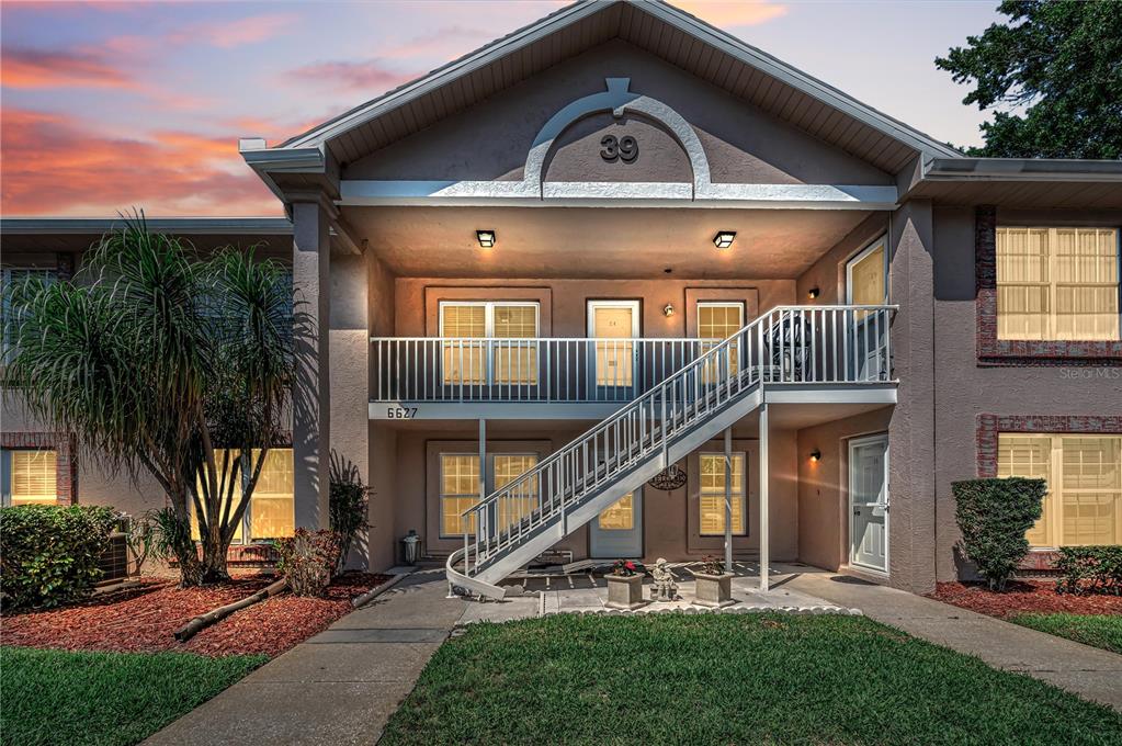 A two-story apartment building exterior features a white metal staircase leading to an upper balcony — 6627 SPRING FLOWER DRIVE UNIT 14, NEW PORT RICHEY, FL