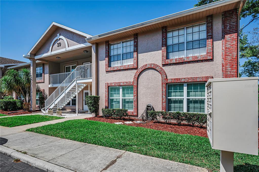 A two-story apartment building with tan stucco walls, brick accents, and an exterior staircase — 6627 SPRING FLOWER DRIVE UNIT 14, NEW PORT RICHEY, FL