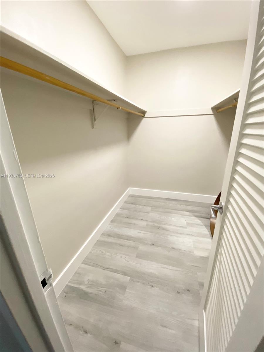 A walk-in closet features light-colored wood-look flooring, white walls, and built-in shelving with hanging rods — 4001 S Ocean Dr # 4M, Hollywood FL 33019, HOLLYWOOD, FL