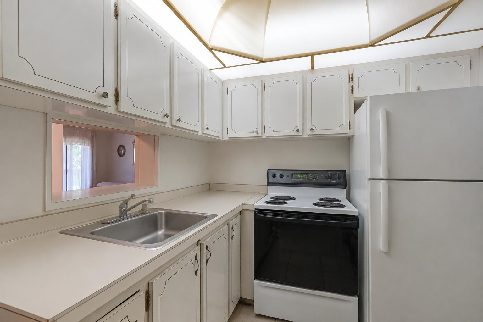 A small kitchen features white cabinets, a stainless steel sink, a stove, and a refrigerator — 16750 NE 14th Avenue # 303, Miami FL 33162, MIAMI, FL