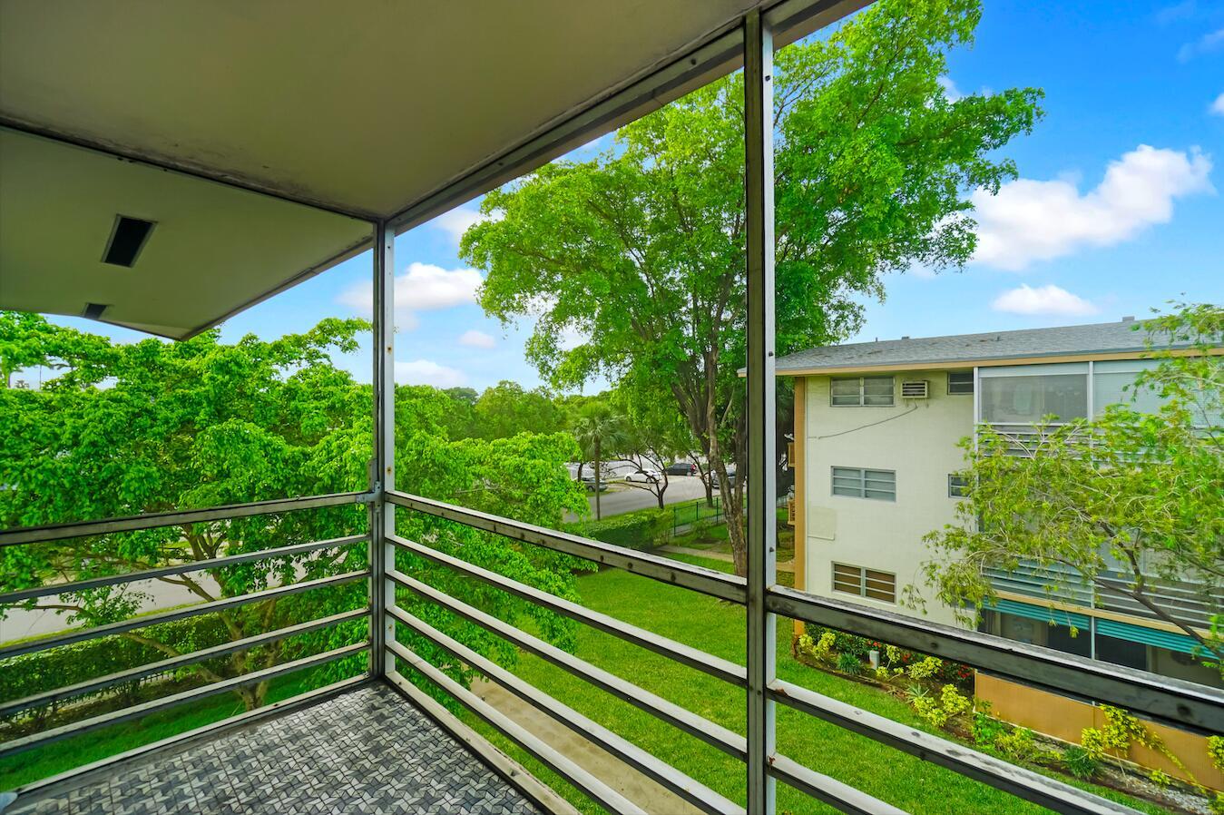A screened-in balcony overlooks a grassy courtyard and a neighboring apartment building — 16750 NE 14th Avenue # 303, Miami FL 33162, MIAMI, FL