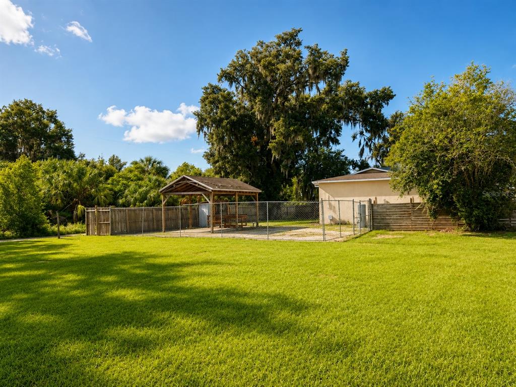 A grassy backyard features a fenced-in gravel area with a wooden pavilion and a house — 7536 TURKEY CREEK ROAD, PLANT CITY, FL