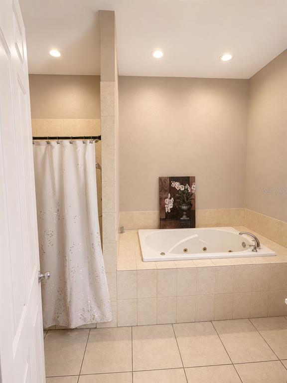 A bathroom features a tiled soaking tub, a shower with a curtain, and beige walls — 7536 TURKEY CREEK ROAD, PLANT CITY, FL