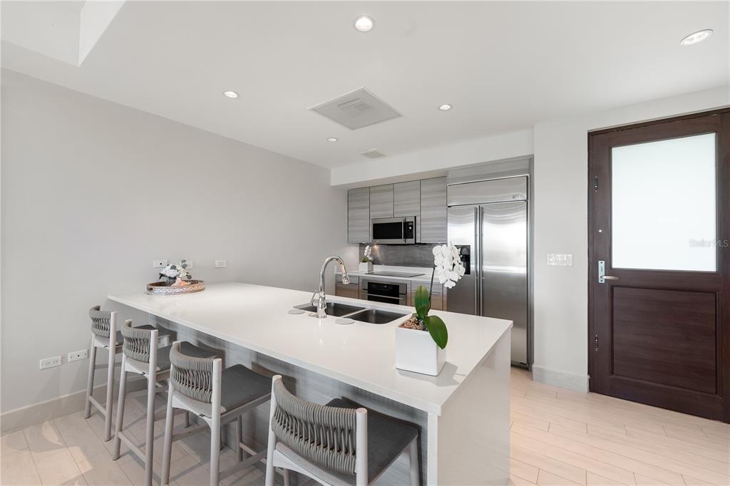 A modern kitchen features a white island with bar seating, stainless steel appliances, and cabinetry — Bahia Beach Golf Club LAS VENTANAS CONDOMINIUM II UNIT 209, RIO GRANDE, PR