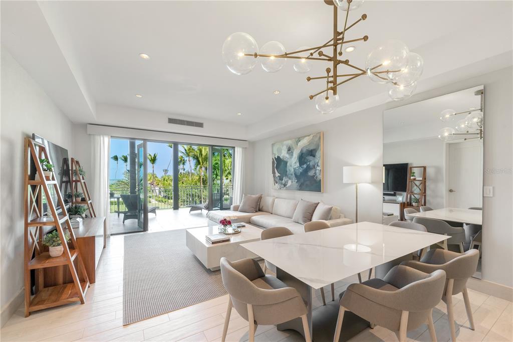A modern living and dining area features a large chandelier, white furniture, and a balcony — Bahia Beach Golf Club LAS VENTANAS CONDOMINIUM II UNIT 209, RIO GRANDE, PR