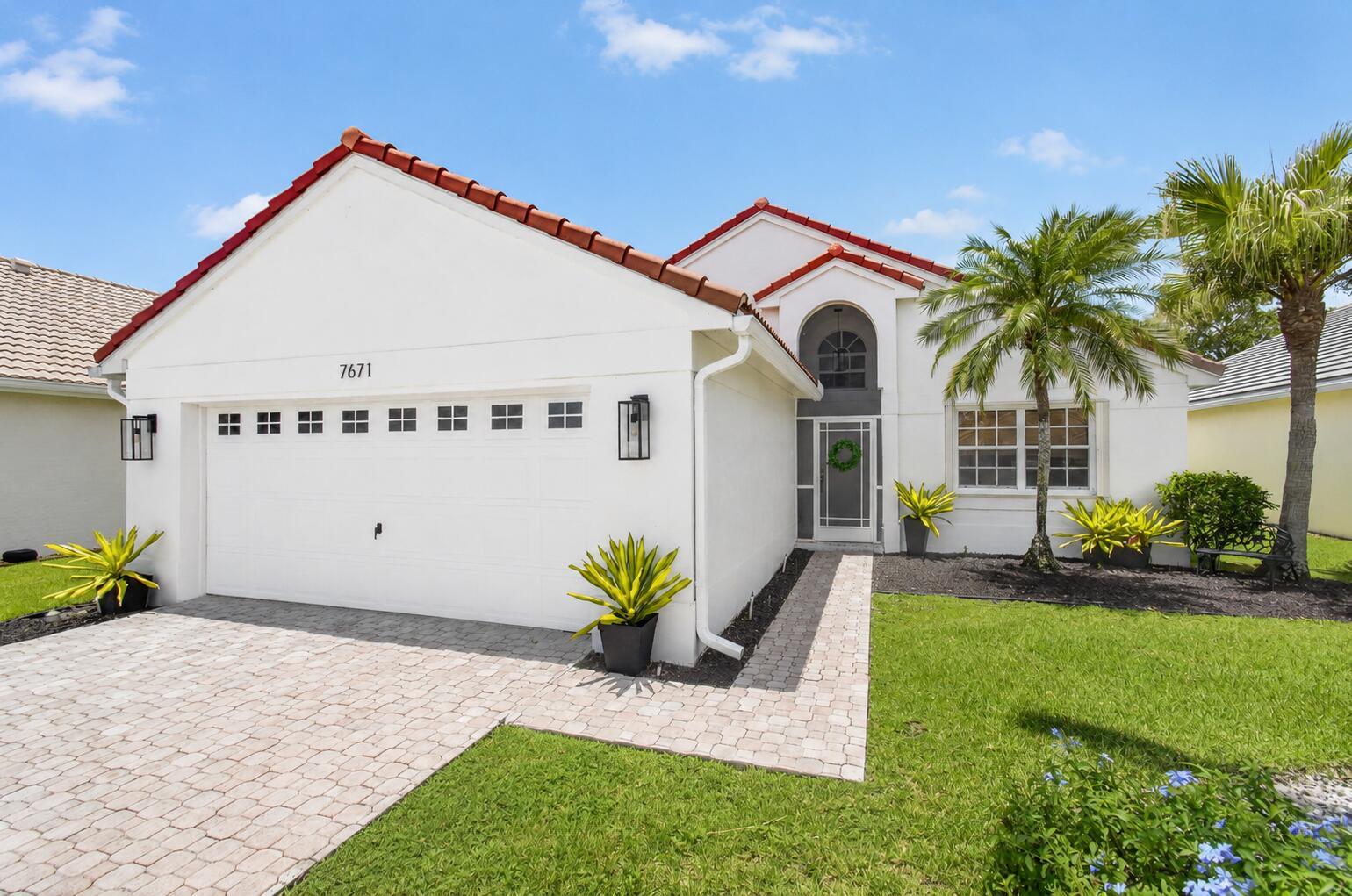A white single-story house with a red tile roof, a two-car garage, and a palm tree — 7671 Stirling Bridge Boulevard N, Delray Beach FL 33446, DELRAY BEACH, FL