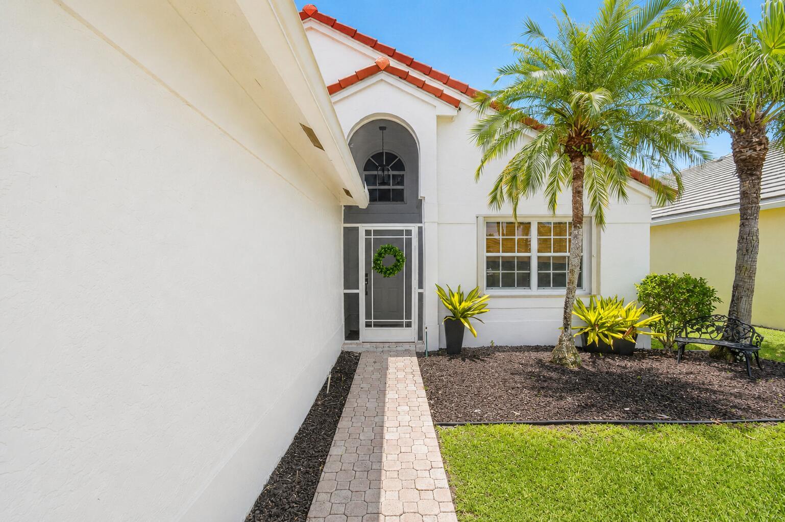 A paved walkway leads to the front entrance of a white house with a palm tree — 7671 Stirling Bridge Boulevard N, Delray Beach FL 33446, DELRAY BEACH, FL