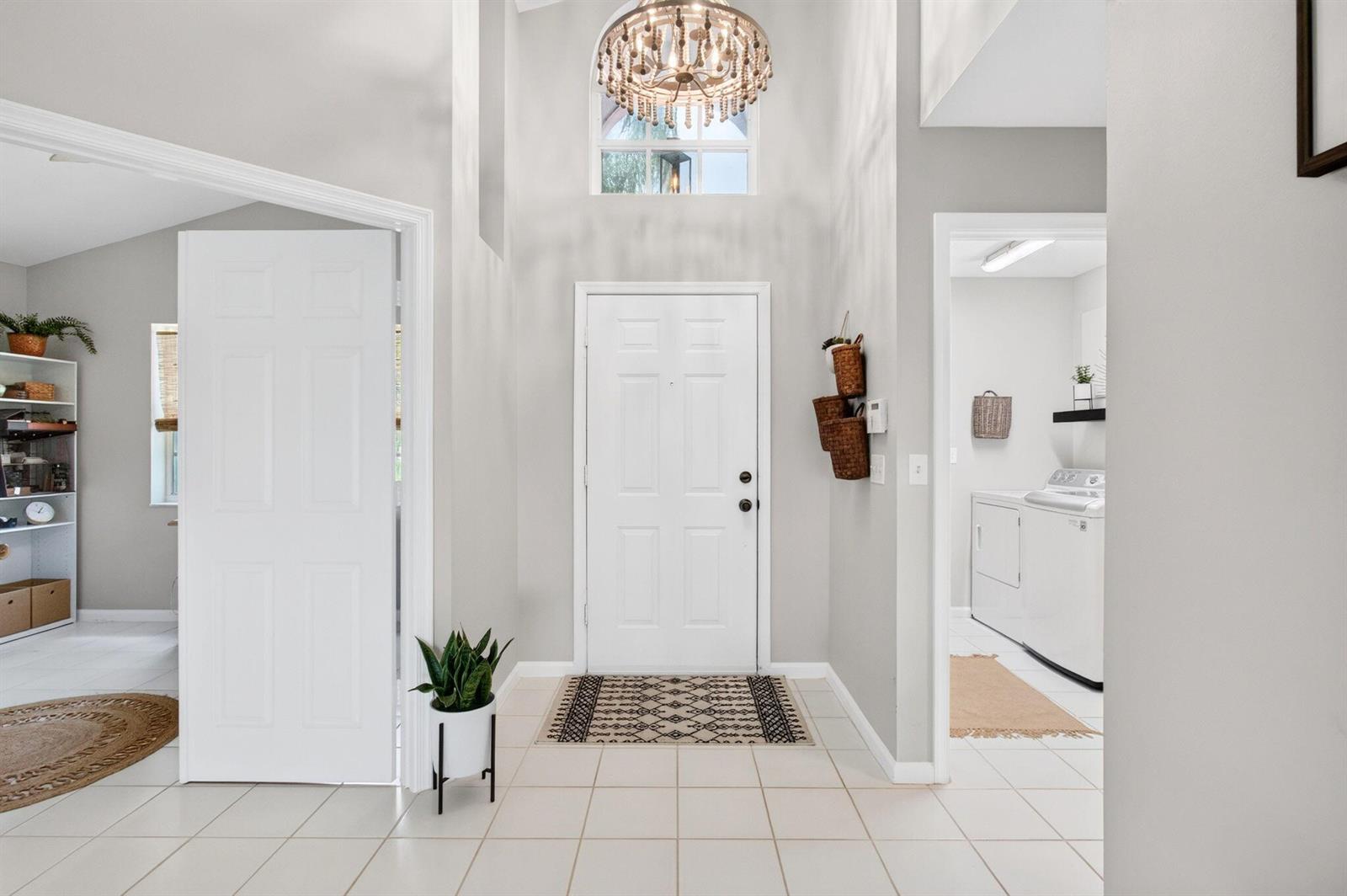 A bright entryway features a white front door, tile flooring, and a beaded chandelier — 7671 Stirling Bridge Boulevard N, Delray Beach FL 33446, DELRAY BEACH, FL