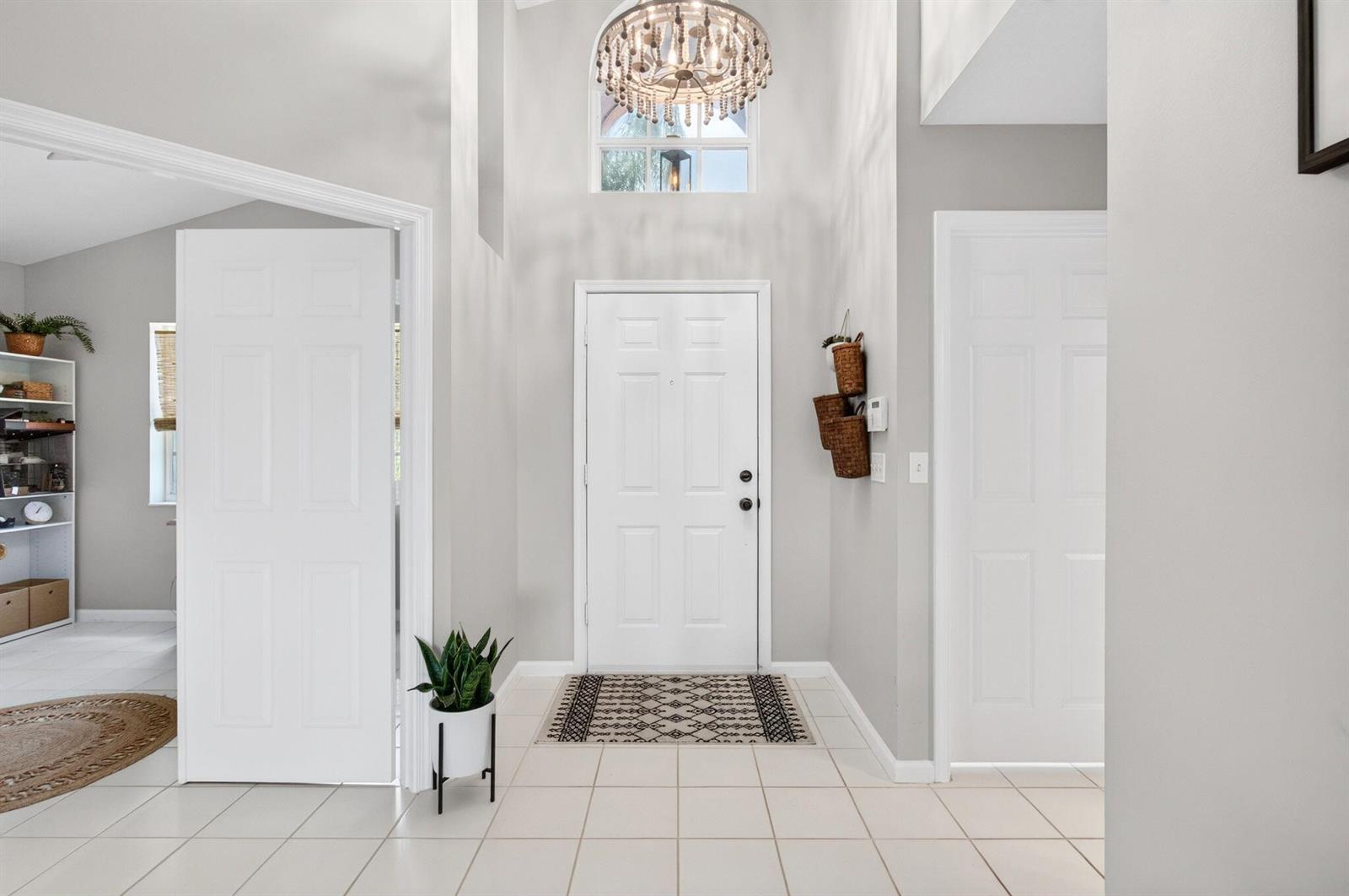 A bright entryway features a white front door, a chandelier, and light-colored tile flooring — 7671 Stirling Bridge Boulevard N, Delray Beach FL 33446, DELRAY BEACH, FL