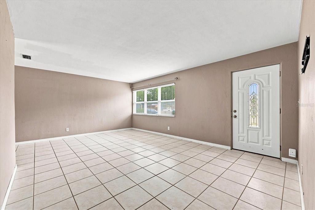 An empty room with beige walls, white tile flooring, a window, and a white front door — 8380 52ND LANE N, PINELLAS PARK, FL