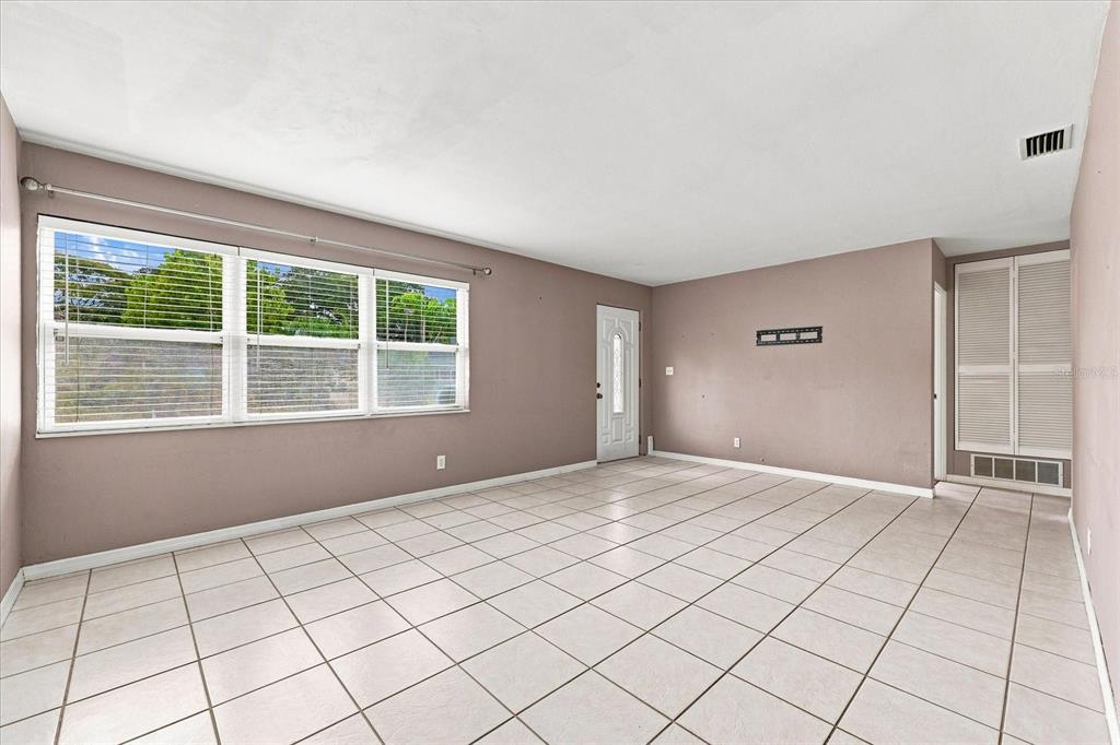 An empty living room with light-colored tile flooring, beige walls, and a large window — 8380 52ND LANE N, PINELLAS PARK, FL