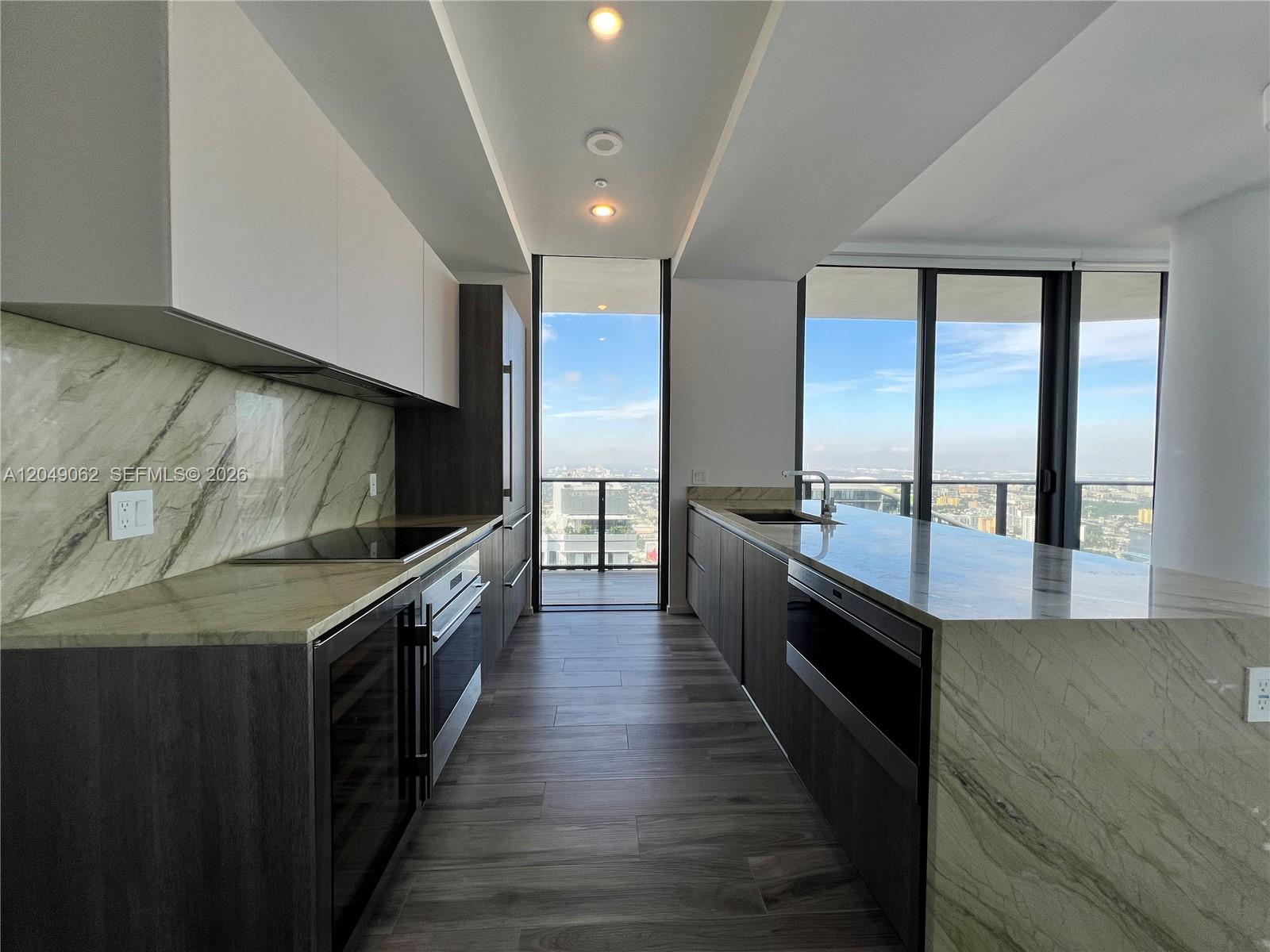 A modern kitchen features dark wood cabinetry, marble countertops, and floor-to-ceiling windows with city views — 801 S Miami Ave # 5309, Miami FL 33130, MIAMI, FL