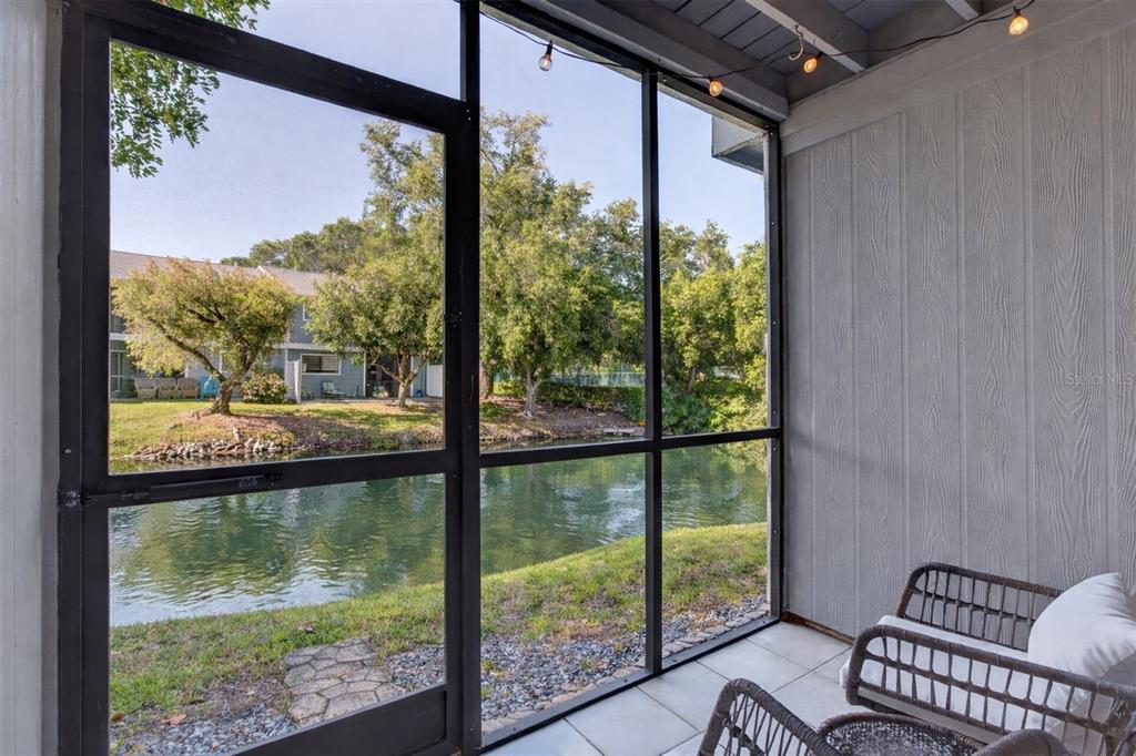 A screened-in patio features tiled flooring, wicker furniture, and a view of a pond — 6033 34TH STREET W UNIT 145, BRADENTON, FL