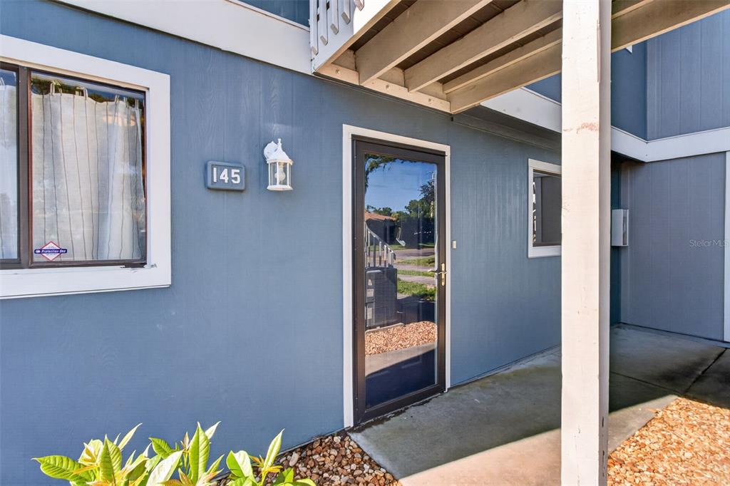 The exterior of a blue building features a front door, a window, and unit number 145 — 6033 34TH STREET W UNIT 145, BRADENTON, FL