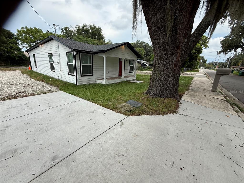 A white house with a red front door sits next to a large oak tree — 225 E WARREN AVENUE, LONGWOOD, FL