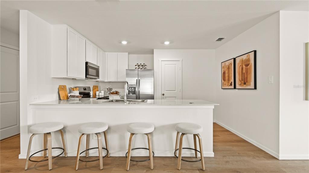 A modern kitchen features white cabinets, stainless steel appliances, a breakfast bar, and four stools — 319 CASTLEVIEW DRIVE, DAVENPORT, FL