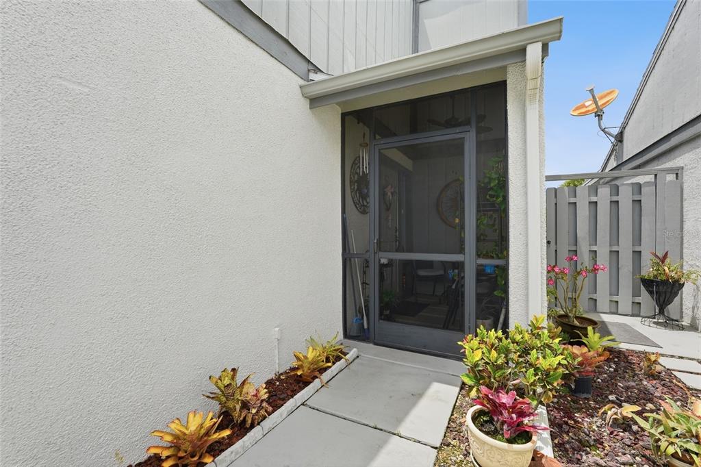 A concrete walkway leads to a screened-in entryway with a white stucco exterior wall — 18441 ORANGECREST COURT, LEHIGH ACRES, FL