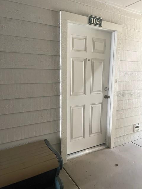 A white six-panel apartment door labeled 104 is set within light-colored horizontal wood siding — 3548 TOBAGO LANE UNIT 104, TAMPA, FL