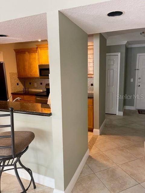 A kitchen with wood cabinets and a breakfast bar overlooks a tiled hallway — 3548 TOBAGO LANE UNIT 104, TAMPA, FL