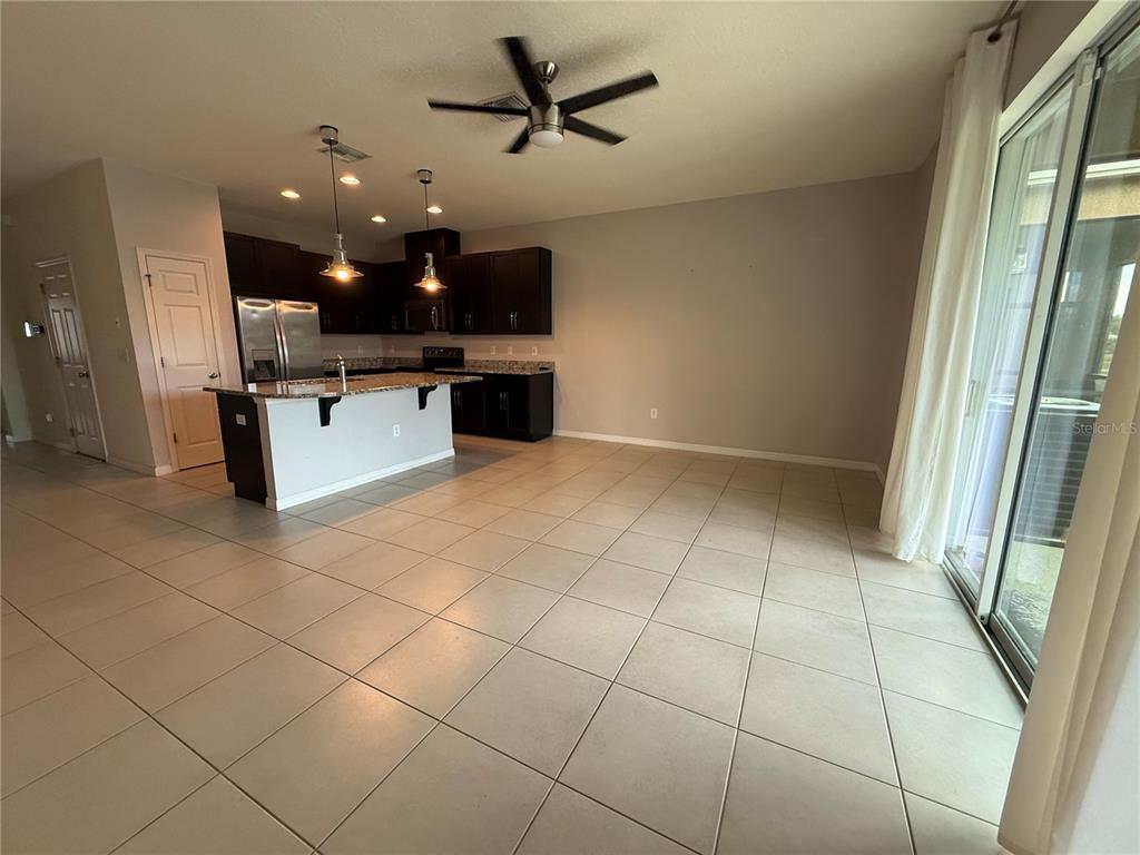 An open-concept kitchen with dark cabinets and a center island overlooks a tiled living area — 6843 40TH LANE N, PINELLAS PARK, FL