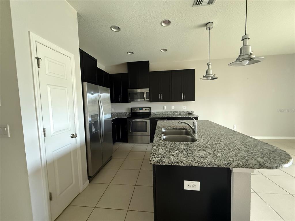 A kitchen features dark cabinets, stainless steel appliances, a granite island, and tile flooring — 6843 40TH LANE N, PINELLAS PARK, FL