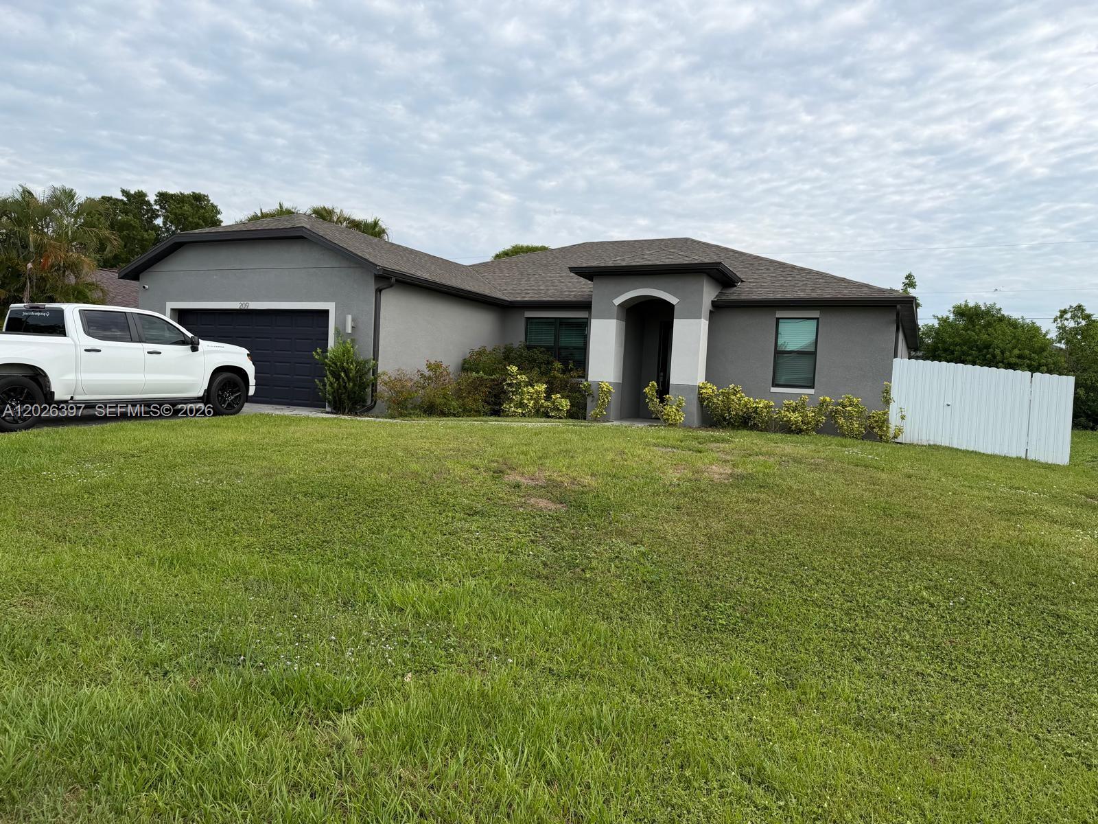 A gray single-story house with a dark garage door and a white fence on the right — 209 SE 26th Ter, Cape Coral FL 33904, CAPE CORAL, FL