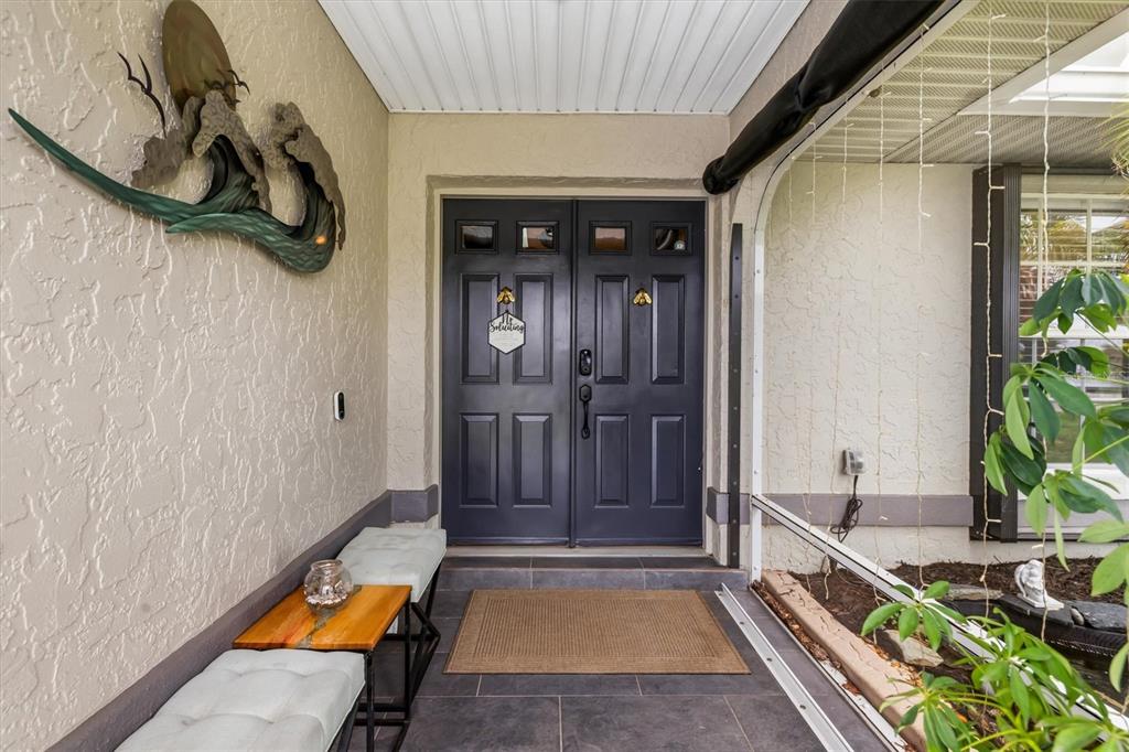 A covered entryway features dark double doors, a tiled floor, and a wall-mounted wave sculpture — 26550 VALPARAISO DRIVE, PUNTA GORDA, FL