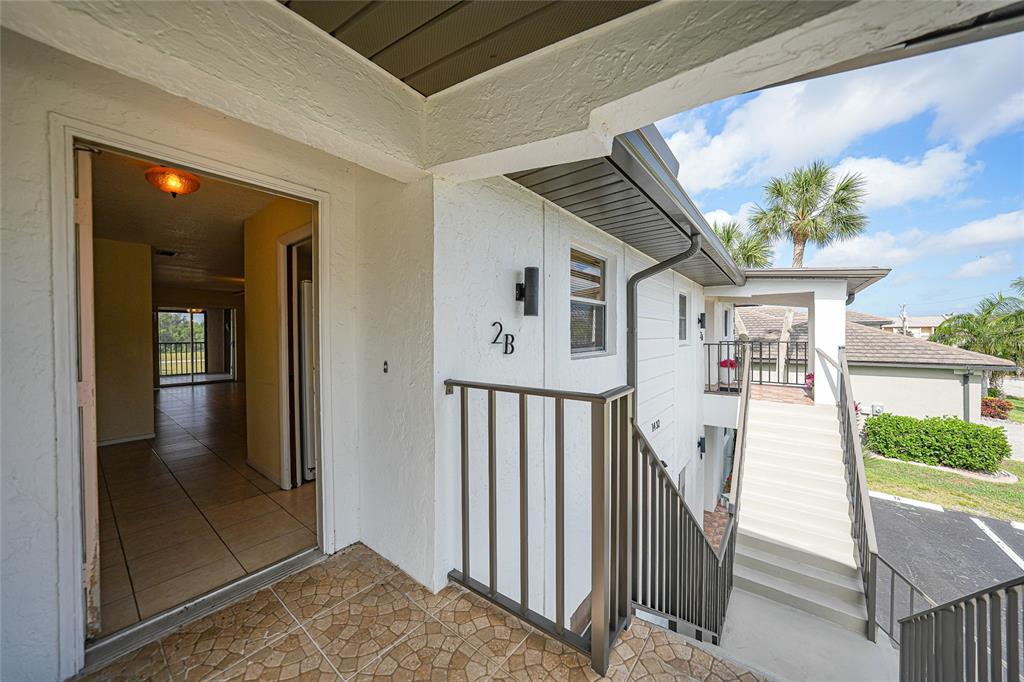 An exterior view of a second-floor apartment entrance with a tiled landing and metal railing — 1432 MEDITERRANEAN DRIVE UNIT 2B, PUNTA GORDA, FL