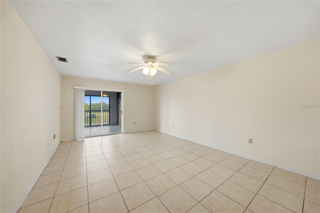 An empty living room features beige tile flooring, a ceiling fan, and a sliding glass door — 1432 MEDITERRANEAN DRIVE UNIT 2B, PUNTA GORDA, FL