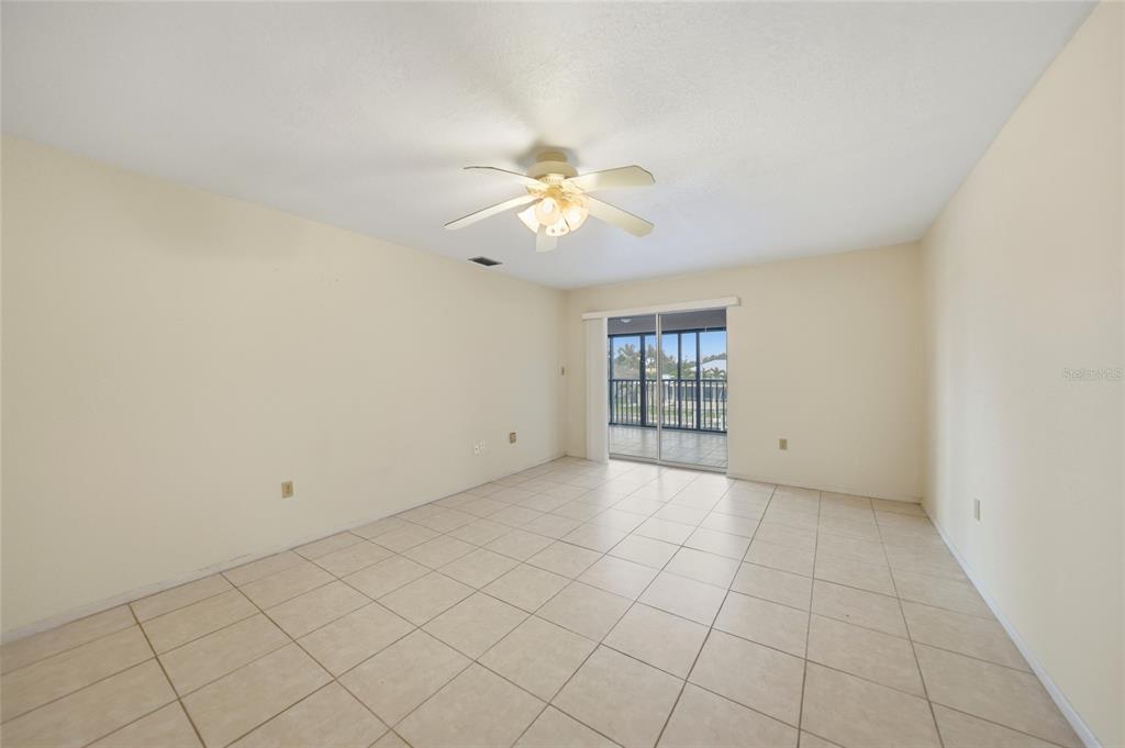 An empty room with beige tile flooring, a ceiling fan, and sliding glass doors — 1432 MEDITERRANEAN DRIVE UNIT 2B, PUNTA GORDA, FL