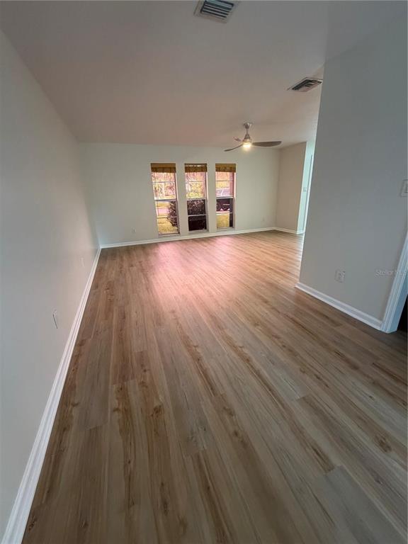 An empty living room features light wood-look flooring, white walls, and three windows — 3024 BLOWN FEATHER LANE, MULBERRY, FL