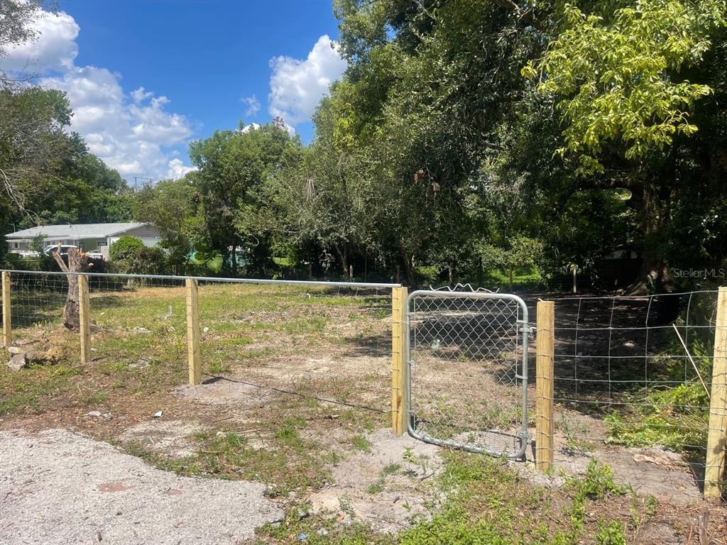 A fenced, vacant lot with a metal gate and mature trees under a blue sky — 25 S MCKINLEY AVENUE, ORLANDO, FL