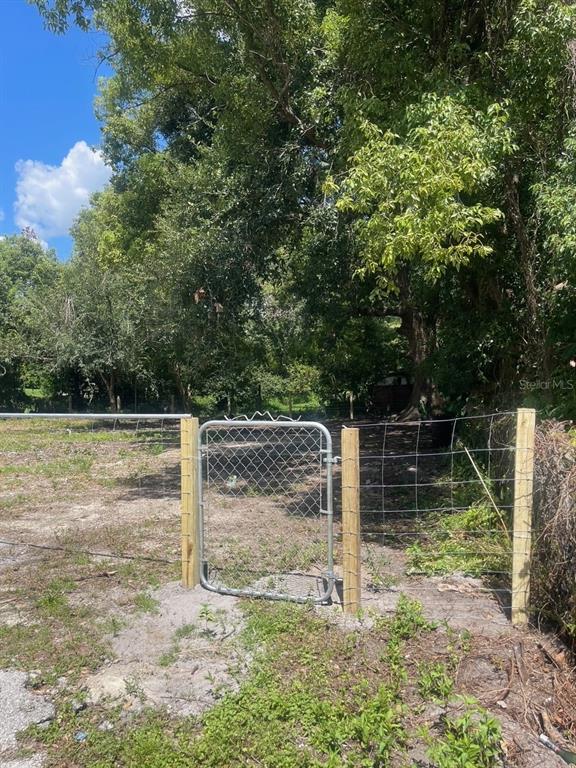 A metal gate is installed in a wire fence bordering a wooded, grassy lot — 25 S MCKINLEY AVENUE, ORLANDO, FL