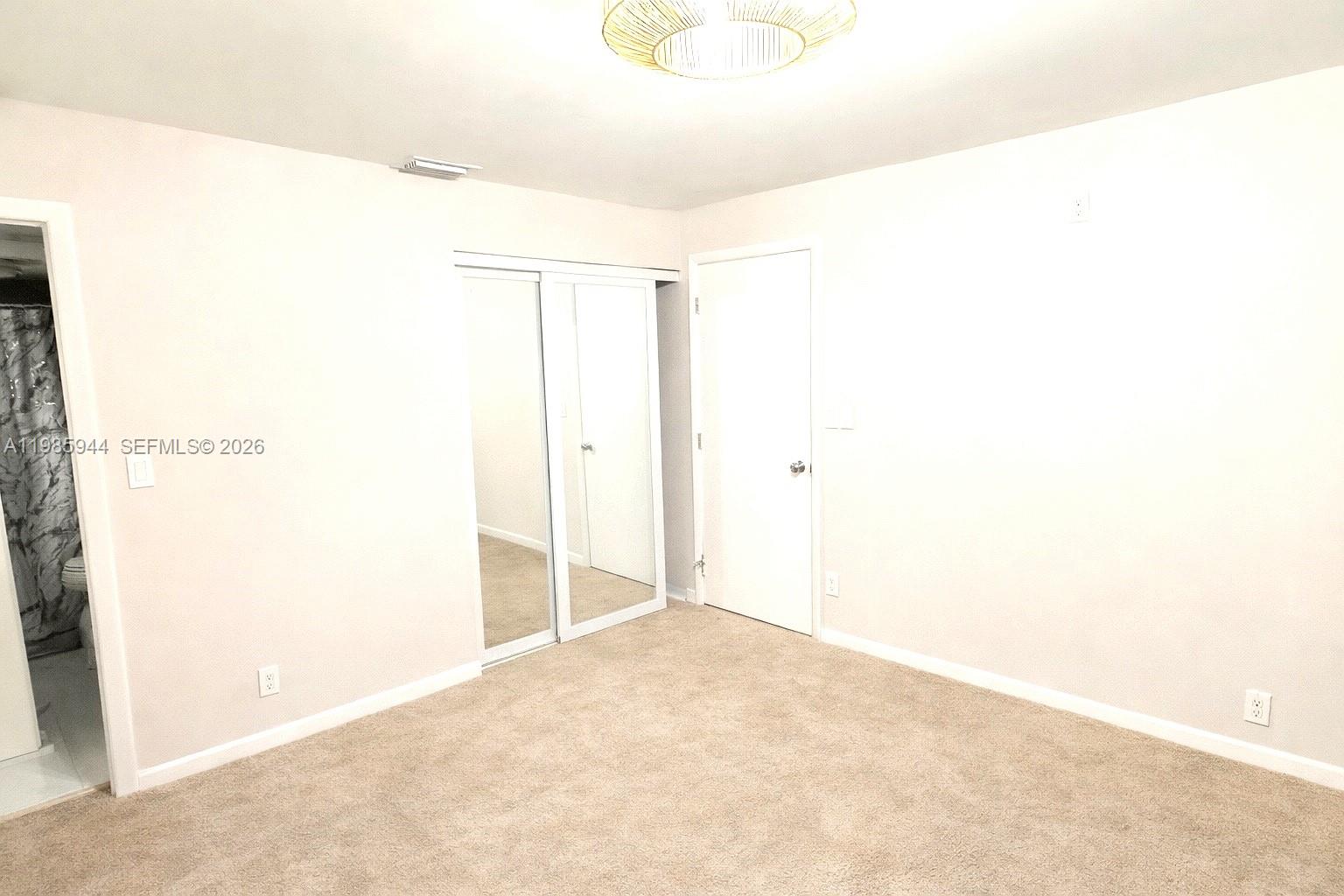 A bedroom features beige carpeting, white walls, a mirrored closet, and a doorway to a bathroom — 7830 NW 33rd St # 308, Davie FL 33024, DAVIE, FL