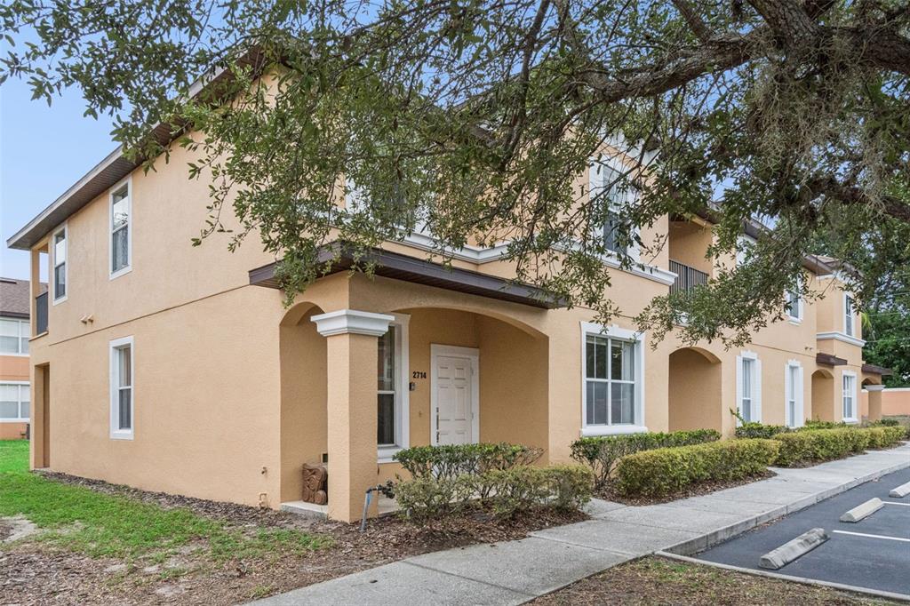 A two-story tan stucco apartment building features a covered entryway and a paved parking lot — 2714 BUSHMAN DRIVE, KISSIMMEE, FL