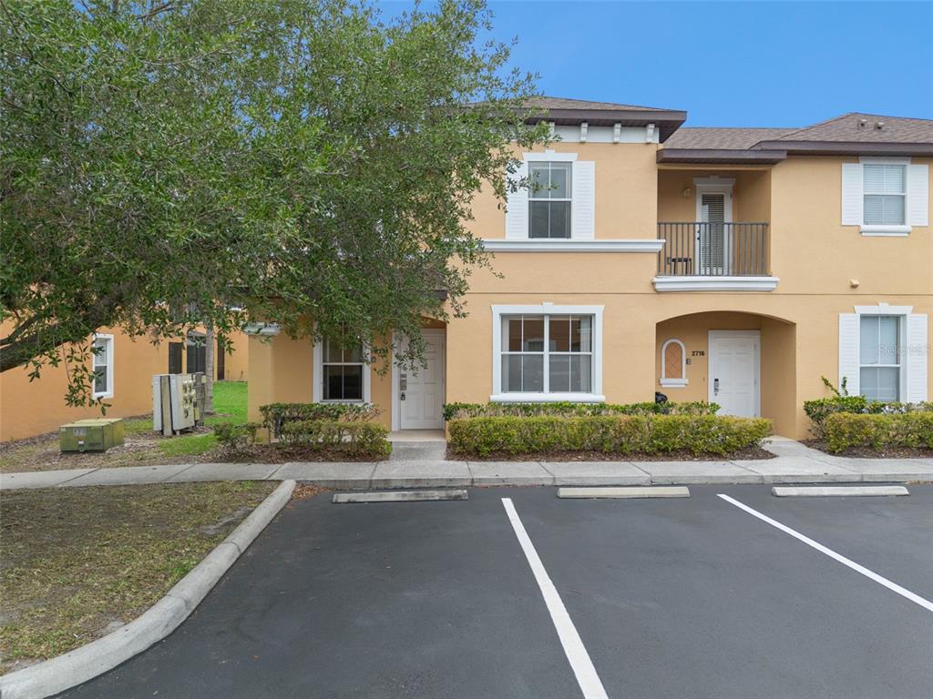 A two-story tan townhouse with a balcony, white trim, and a parking lot in front — 2714 BUSHMAN DRIVE, KISSIMMEE, FL