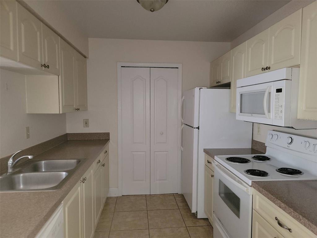 A kitchen features white cabinets, laminate countertops, a double sink, and white appliances — 2550 N ALAFAYA TRAIL UNIT 2103, ORLANDO, FL