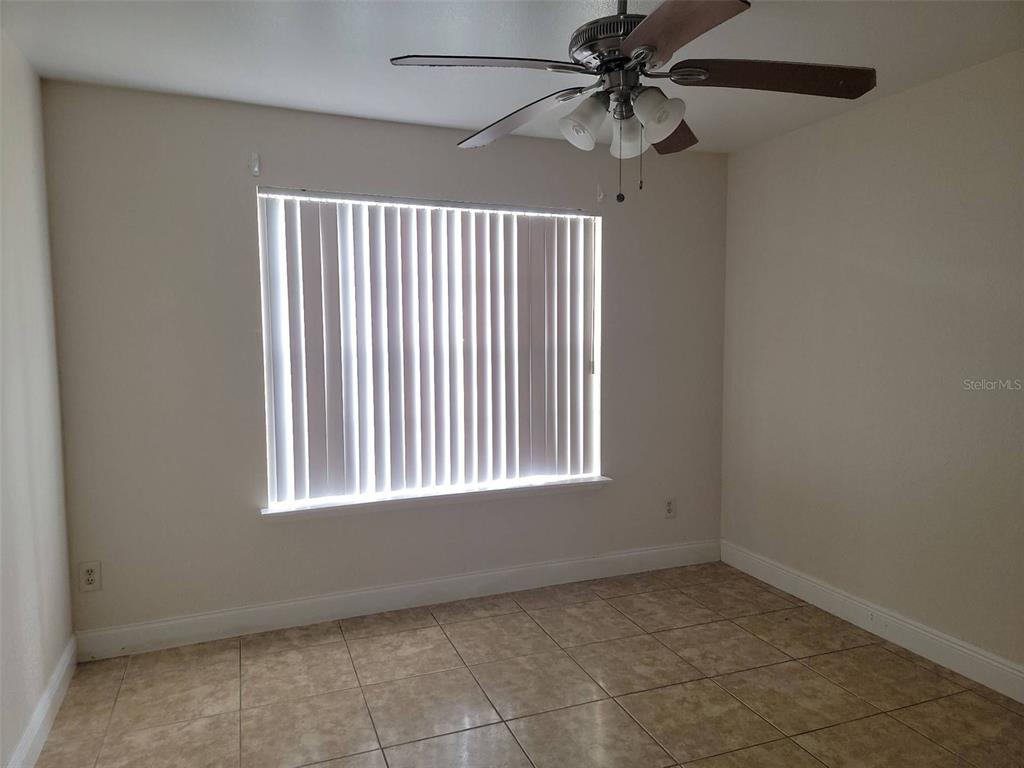 An empty room with beige walls, tile flooring, a ceiling fan, and vertical window blinds — 2550 N ALAFAYA TRAIL UNIT 2103, ORLANDO, FL