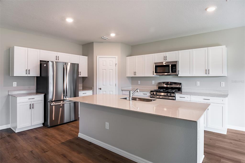 A modern kitchen features white cabinetry, stainless steel appliances, and a large central island — 36613 SAGEMOOR DRIVE, ZEPHYRHILLS, FL