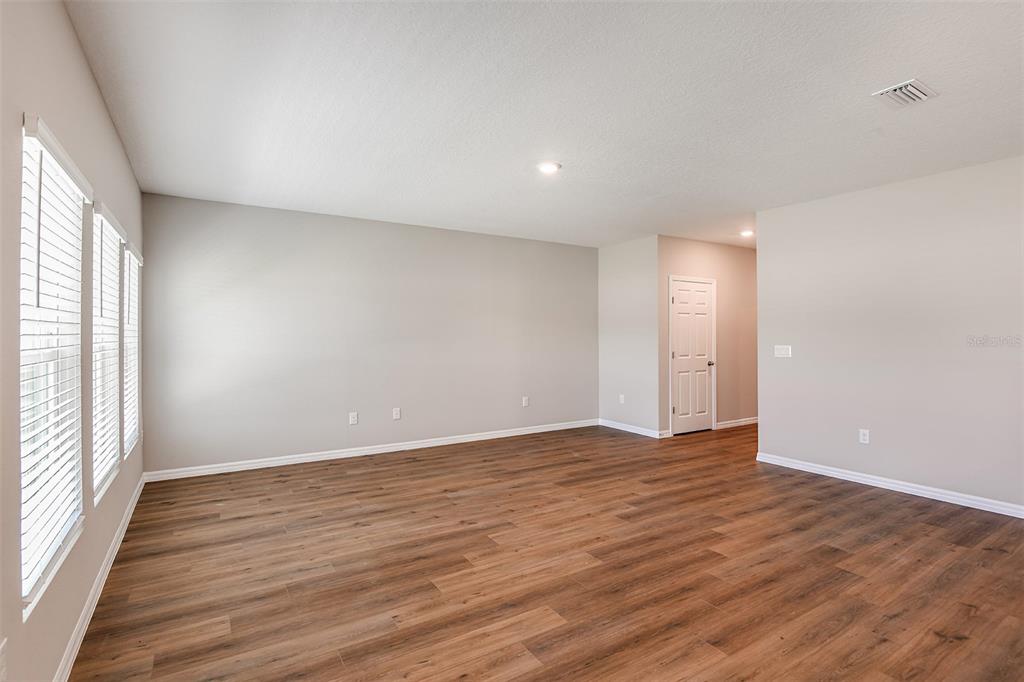 An empty room with light gray walls, wood-look flooring, and three windows with blinds — 36613 SAGEMOOR DRIVE, ZEPHYRHILLS, FL